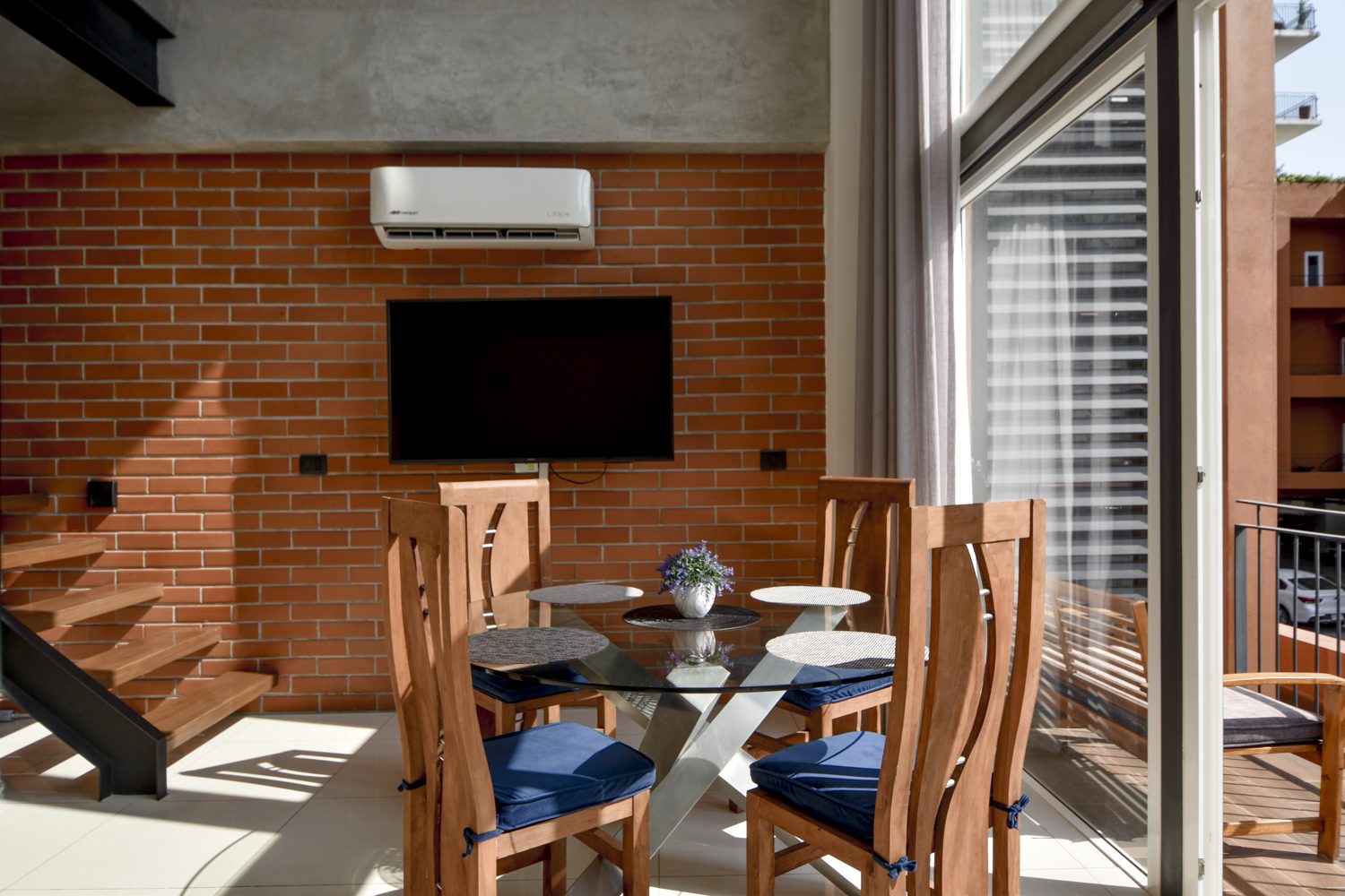 Dining area against the exposed brick wall with mounted TV and direct balcony access
