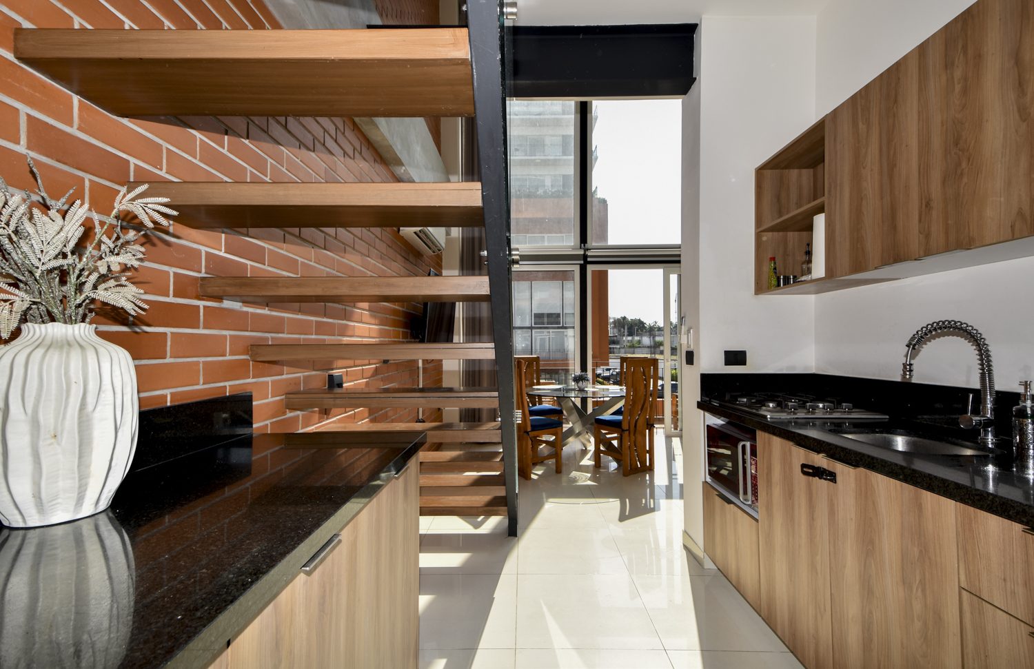 Floating wood staircase against the exposed brick wall beside the granite kitchen